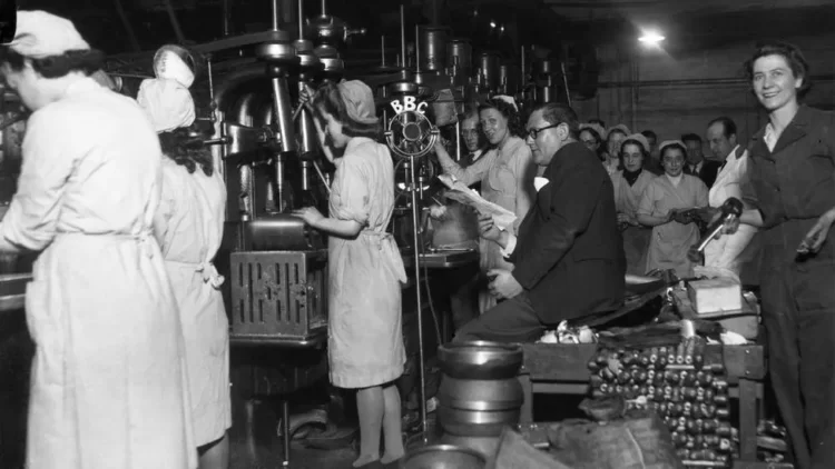 Victor Smythe reads a radio script at a munitions factory in Manchester